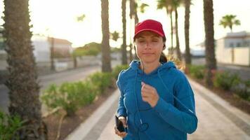 donna con cuffie corre giù il strada lungo il palma viale a tramonto. salutare attivo stile di vita. lento movimento video