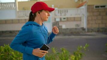 vrouw met hoofdtelefoons loopt naar beneden de straat langs de palm Laan Bij zonsondergang. gezond actief levensstijl. langzaam beweging video