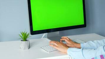 mujer mecanografía en un computadora teclado a hogar oficina, monitor con un verde pantalla. croma llave. Copiar espacio. concepto de remoto trabajar. video