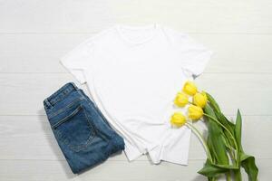 blanco camiseta Bosquejo. modelo blanco camisa parte superior vista. blanco de madera antecedentes. madre mujer día día festivo. amarillo tulipanes mujer camiseta con cumpleaños ramo de flores flores primavera mirar. hembra accesorios foto