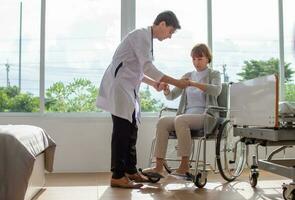 caucasian man doctor is examining the female older patient in wheelchair the hospital. photo