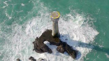 Leuchtturm auf ein Felsen im das Ozean mit abstürzen Wellen und ein Hubschrauberlandeplatz video