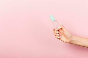 Female hand holding cream bottle of lotion isolated. Girl give tube cosmetic products on pink background photo