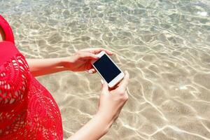 Close up hand of woman holding smartphone and take photo standing in the sea