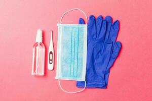 Top view of alcohol hand sanitizer, latex gloves, digital thermometer and medical mask on pink background. Virus protection equipment concept with copy space photo