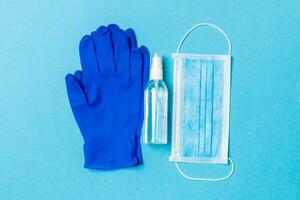 Top view of protective medical equipment such as surgical mask, hand alcohol sanitizer and latex gloves on blue background. Health care concept with copy space photo