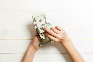 Top view of a businesswoman's hands counting different dollar banknotes on wooden background. Success and wealth concept photo