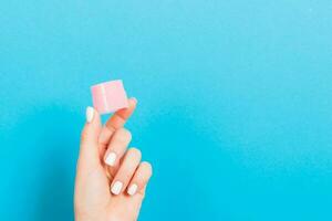 Female hand holding cream bottle of lotion isolated. Girl give jar cosmetic products on blue background photo