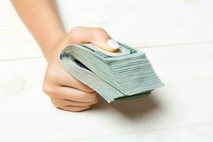 Perspective view of female hand holding a pack of money on wooden background. One hundred dollars. Business concept. Charity and tips concept photo