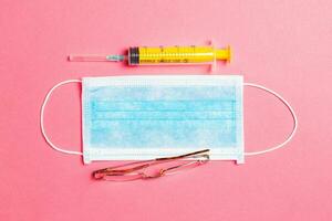 Top view of protective medical mask, syringe and eye glasses on pink background. Prevention of virus infection concept with copy space photo