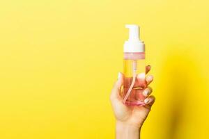 Female hand holding spray cream bottle of lotion isolated. Girl give cosmetic products on yellow background photo