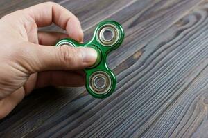 A man's hand holding and playing metal green color fidget spinner with wooden table background photo