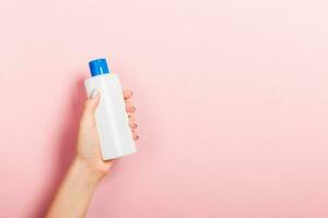 Female hand holding cream bottle of lotion isolated. Girl give tube cosmetic products on pink background photo