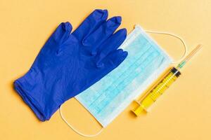 Top view of disposable surgical mask, pair of latex medical gloves and syringe on orange background. Protect your health concept with copy space photo