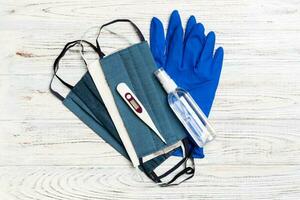 Top view of alcohol hand sanitizer, latex gloves, digital thermometer and handmade reusable masks on wooden background. Virus protection equipment concept with copy space photo