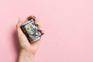 Female hand holding tightly a rolled bundle of money. Top view of one hundred dollars on colorful background. Investment concept with copy space photo