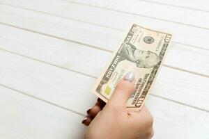Female hand holding ten hundred dollar banknote on wooden background. Salary and wage concept with copy space photo