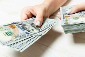 Female hand giving one hundred dollar banknotes on wooden background. Perspective view of wealth concept photo