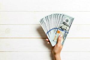 Fan of one hundred dollar bills in female hand on wooden background. Investment concept photo