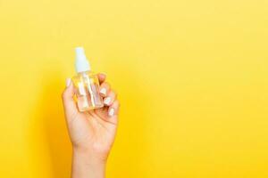 Female hand holding spray cream bottle of lotion isolated. Girl give cosmetic products on yellow background photo