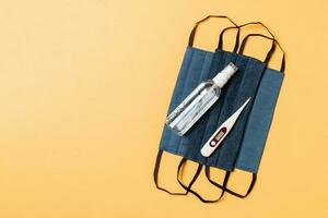 Top view of handmade cotton masks, alcohol hand sanitizer and digital thermometer on orange background with copy space. Protective medical equipment concept photo