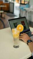 Man using a laptop and a glass of orange juice in a cafe photo