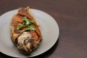 The fried tilapia was just right. Served in gray work on a brown wooden table. photo