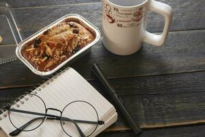 Banana Cake on a black wooden table With note book, glasses, and coffee mugs. photo