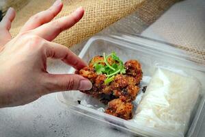 Hand picked fried pork and wrapped sticky rice Placed in a plastic takeaway box, on a white table. photo