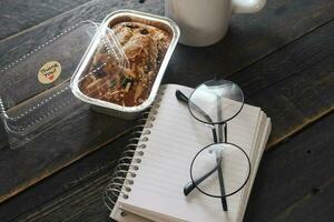 Banana Cake on a black wooden table With note book, glasses, and coffee mugs. photo