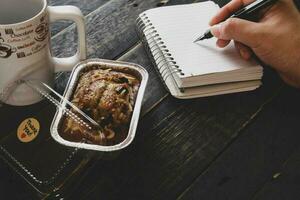 Banana Cake on a black wooden table With note book, glasses, and coffee mugs. photo