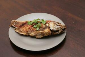 The fried tilapia was just right. Served in gray work on a brown wooden table. photo