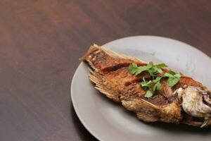 The fried tilapia was just right. Served in gray work on a brown wooden table. photo