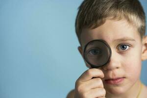 Cute Caucasian boy with a magnifying glass at the eye. funny boy looking through magnifying glass. photo