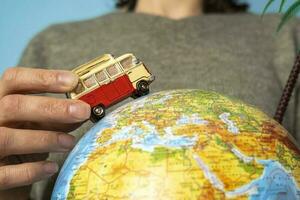 The concept of road trips - a toy car rides on a globe in the hands of a girl photo