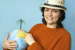 A pretty woman in a sun hat holds a globe in her hands and shows a vacation spot photo