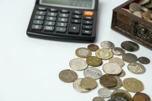 calculadora, pecho, monedas en un blanco antecedentes. el concepto de ahorros foto