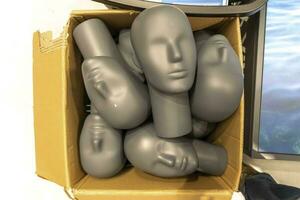 gray plastic mannequin heads are in a cardboard box photo