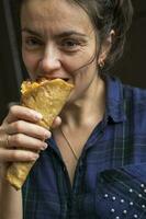 A pretty middle-aged woman in a purple plaid shirt is eating a pizza cone. Fast food. Delicious pizza photo