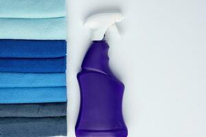 A purple bottle of cleanser with a spray and colored cleaning cloths on a white background photo