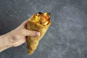 Pizza cone in a woman's hand on a dark gray background. photo