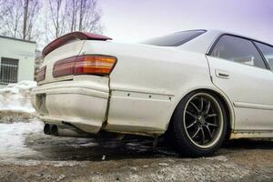 the back of a white smashed Japanese sedan with black rims photo