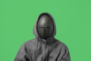 an unrecognizable man in a gray hoodie with a mask on his face isolated on a green background photo