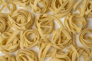 Raw tagliatelle , nest pasta, Egg pasta nests lying in a pattern on a white background, the pattern is a top view photo