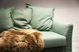 Light green sofa with pillows, plaid and fur cape, Living room furniture photo