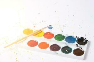 coloque pintura de acuarela brillante y un pincel para pintar con acuarela con manchas de fondo blanco. foto