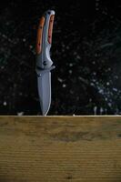 cuchillo plegable para supervivencia viga de madera atascada, sobre fondo oscuro. foto