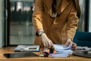 mujer de negocios manos trabajando en pilas de papel documentos a buscar y revisión documentos apilado en mesa antes de enviando ellos a tablero de directores a utilizar correcto documentos en reunión con empresario foto