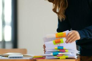 mujer de negocios manos trabajando en pilas de papel documentos a buscar y revisión documentos apilado en mesa antes de enviando ellos a tablero de directores a utilizar correcto documentos en reunión con empresario foto