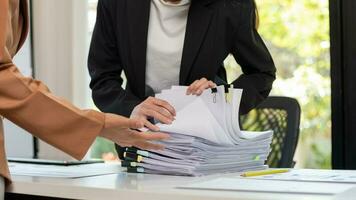 mujer de negocios manos trabajando en pilas de papel documentos a buscar y revisión documentos apilado en mesa antes de enviando ellos a tablero de directores a utilizar correcto documentos en reunión con empresario foto